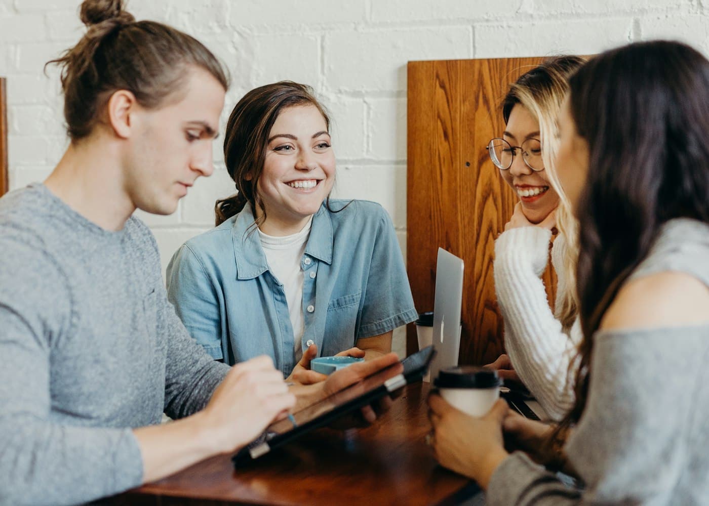 Four people sitting at a wooden table, talking and smiling over coffee.
