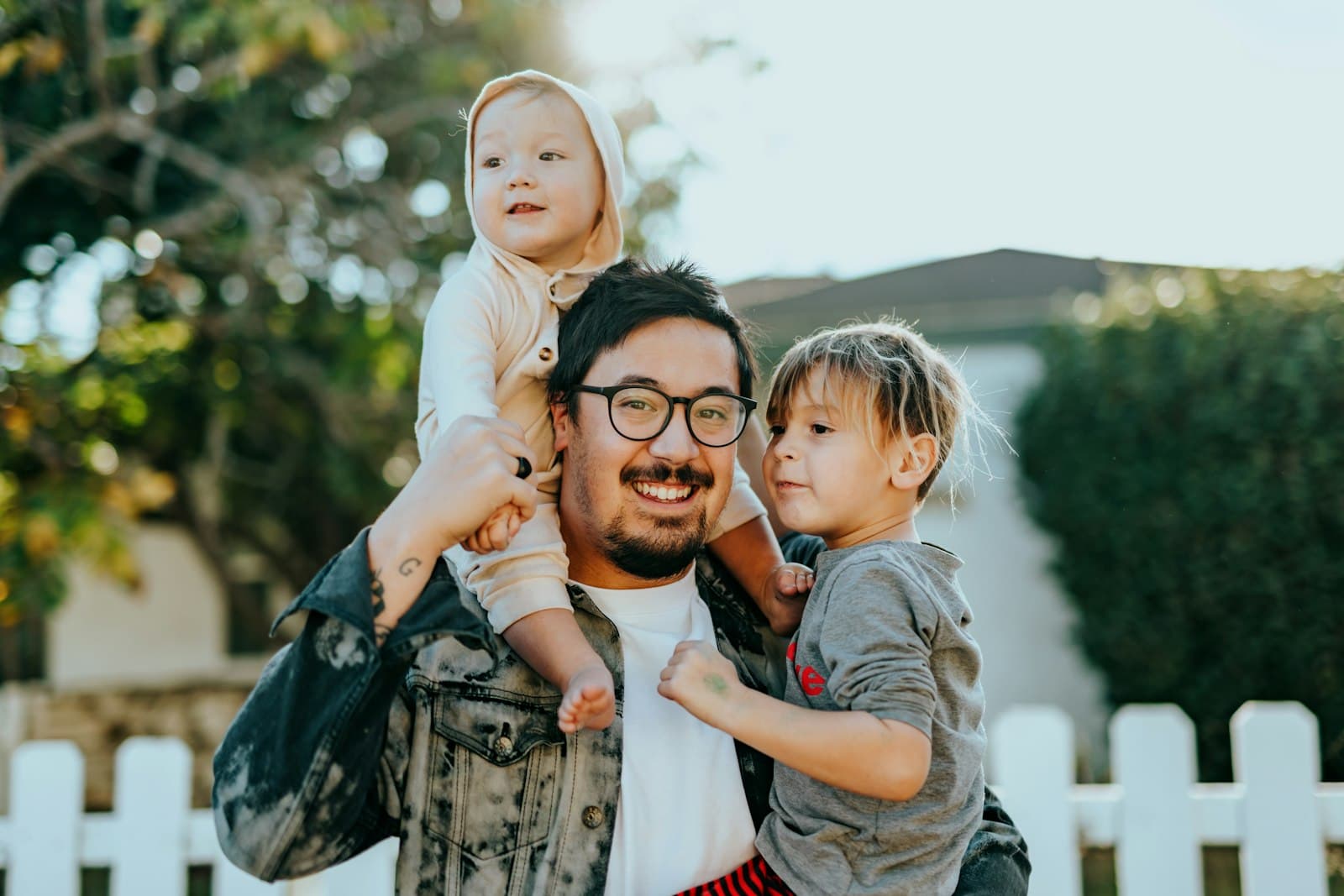 A parent smiling outdoors with two young children.