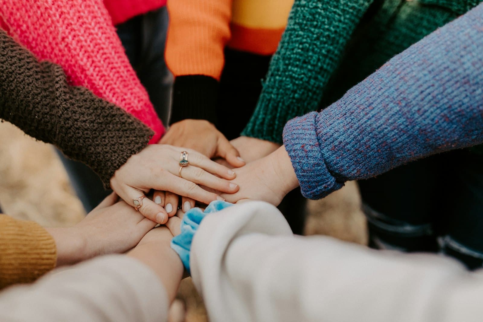 Several people stacking their hands together, wearing colourful sweaters.